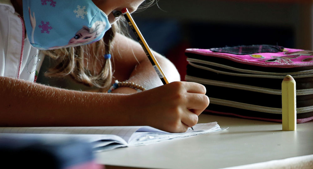 Девочка в маске пишет задание на уроке в школе 