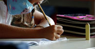 Девочка в маске пишет задание на уроке в школе 