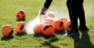 Тренер обрабатывает антисептиком  мячи на футбольном поле перед началом тренировки 