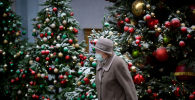 Пожилая женщина в маске идет мимо наряженных новогодних елок