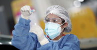 Медик в защитном костюме изучает содержимое пробирки с ПЦР-тестом на коронавирус