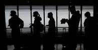 Люди в защитных костюмах стоят в очереди на регистрацию в аэропорту 