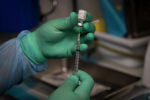 Медик в защитном костюме готовит шприц с вакциной от коронавируса 