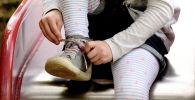 Девочка завязывает шнурки на ботинках