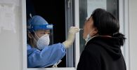 Медик в защитном костюме берет пробу для ПЦР-теста на коронавирус