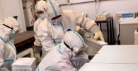 Медики в защитных костюмах укладывают вакцину от коронавируса в холодильники