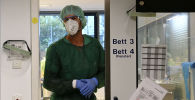 Медик в защитном костюме стоит в дверях отделения реанимации