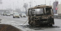 Машины двигаются по улице, на которой стоит разбитый и сожженный автобус