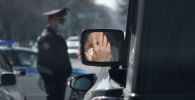 Мужчина в защитной маске отражается в боковом зеркале автомобиля в Алматы