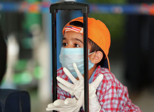 Ребенок в защитной маске и перчатках опирается на чемодан в ожидании рейса