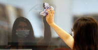 Девушка в маске протирает стекло в кафе после ослабления карантина 