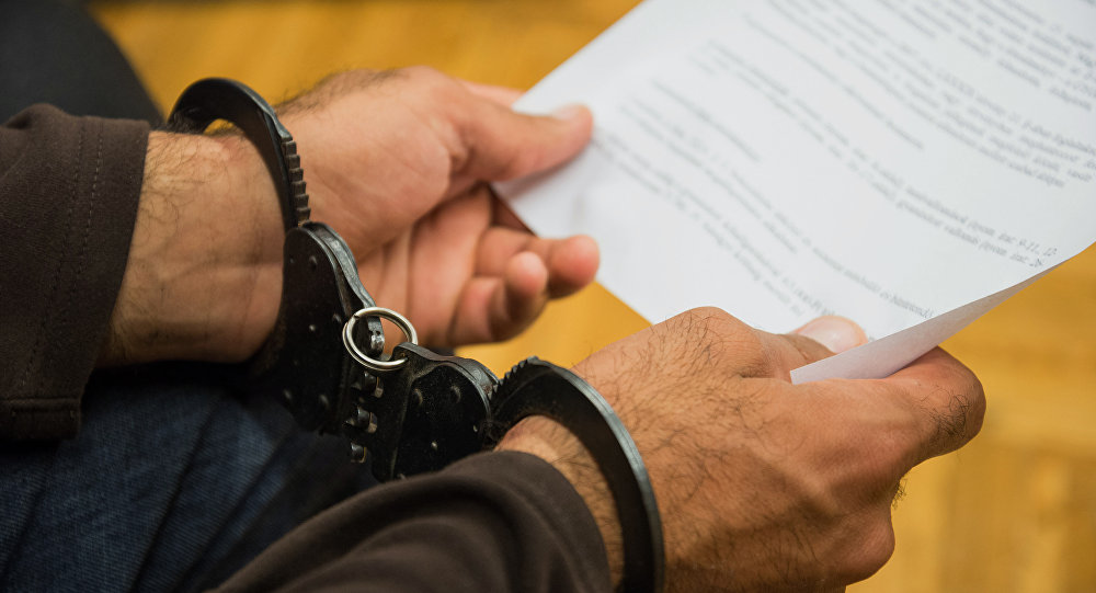Человек в наручниках держит официальный документ, фото из архива