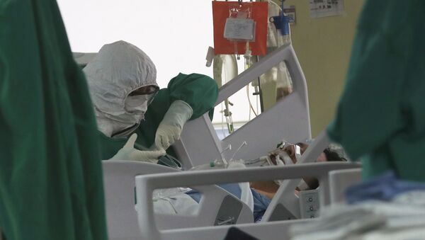 Медик в защитном костюме наблюдает за пациентом в палате интенсивной терапии в больнице с коронавирусом - Sputnik Казахстан