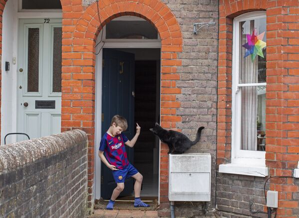Юный футболист на пороге своего дома и соседский кот, заглядывающий через дверь, Великобритания - Sputnik Казахстан