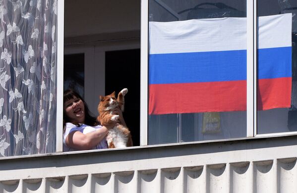 Жительница Красноярска со своим котом смотрит выступление музыкального ансамбля в День России из окна своей квартиры - Sputnik Казахстан