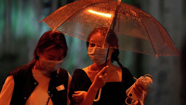 Девушки в защитных масках гуляют под зонтом дождливым вечером - Sputnik Казахстан