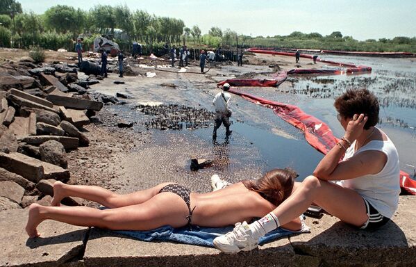 Отдыхающие рядом с рабочими во время очистки пляжа от нефти в Аргентине, 1999 год  - Sputnik Казахстан