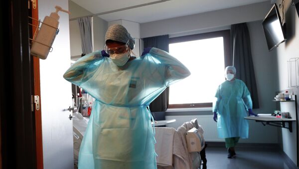 Медик поправляет защитный костюм, выходя из палаты в больнице с коронавирусом - Sputnik Казахстан