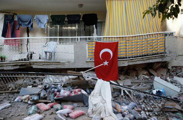 Турецкий флаг виден возле поврежденного здания после землетрясения в портовом городе Измир на Эгейском море, Турция - Sputnik Қазақстан