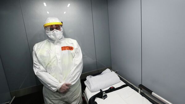 Медик в защитном костюме едет в лифте с носилками для пациента с коронавирусом  - Sputnik Казахстан