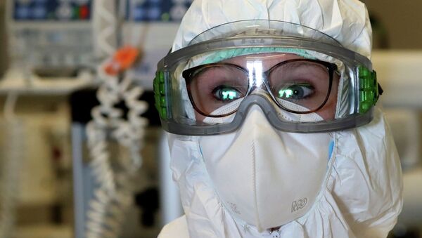 Врач в защитном костюме рассматривает показания медицинской аппаратуры в больнице с коронавирусом - Sputnik Казахстан