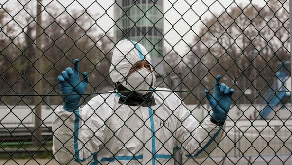Медик в защитном костюме стоит у сетчатой ограды  - Sputnik Қазақстан