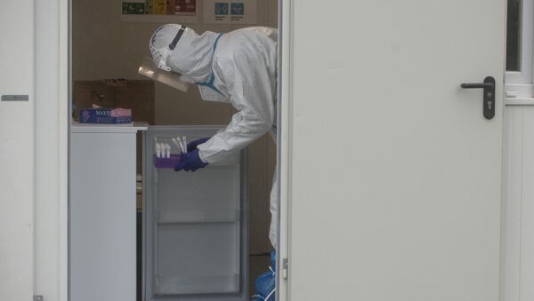 Медик в защитном костюме ставит пробирки с пробами на коронавирус в холодильник  - Sputnik Казахстан
