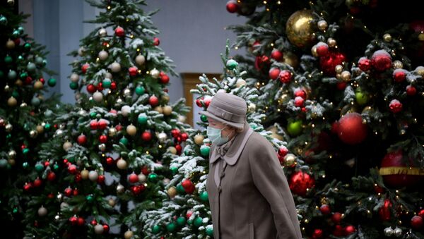 Пожилая женщина в маске идет мимо наряженных новогодних елок - Sputnik Казахстан