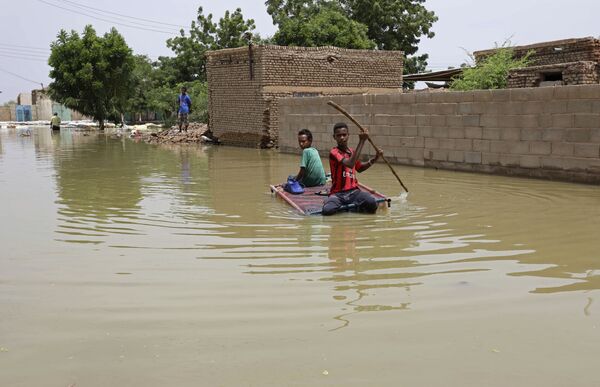 Подростки плывут на плоту по затопленной в результате наводнения улице в городе Салмания, Судан - Sputnik Казахстан
