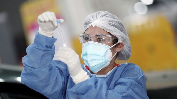 Медик в защитном костюме изучает содержимое пробирки с ПЦР-тестом на коронавирус - Sputnik Қазақстан
