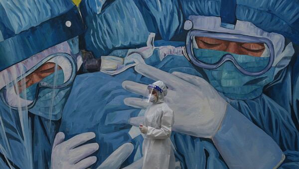 Медик в защитном костюме стоит у стены с муралом, посвященным врачам  - Sputnik Казахстан