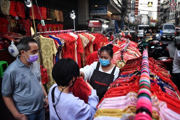 Торговец помогает покупателям выбрать одежду перед празднованием Лунного Нового года в китайском квартале Бангкока, Таиланд - Sputnik Қазақстан