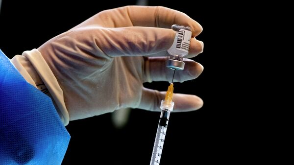 Медик у защитном костюме шприцом набирает вакцину  - Sputnik Қазақстан