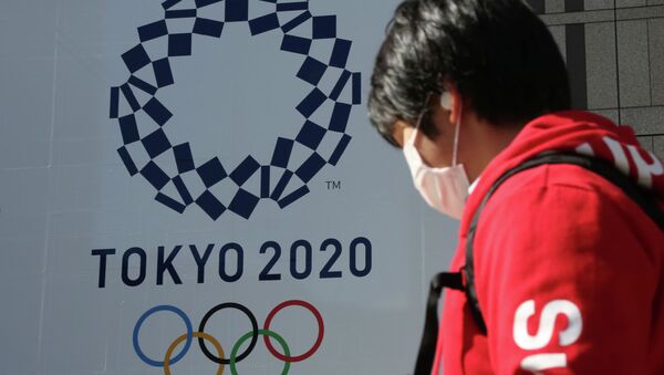 Человек в маске проходит мимо плаката с символикой Олимпиады в Токио  - Sputnik Казахстан