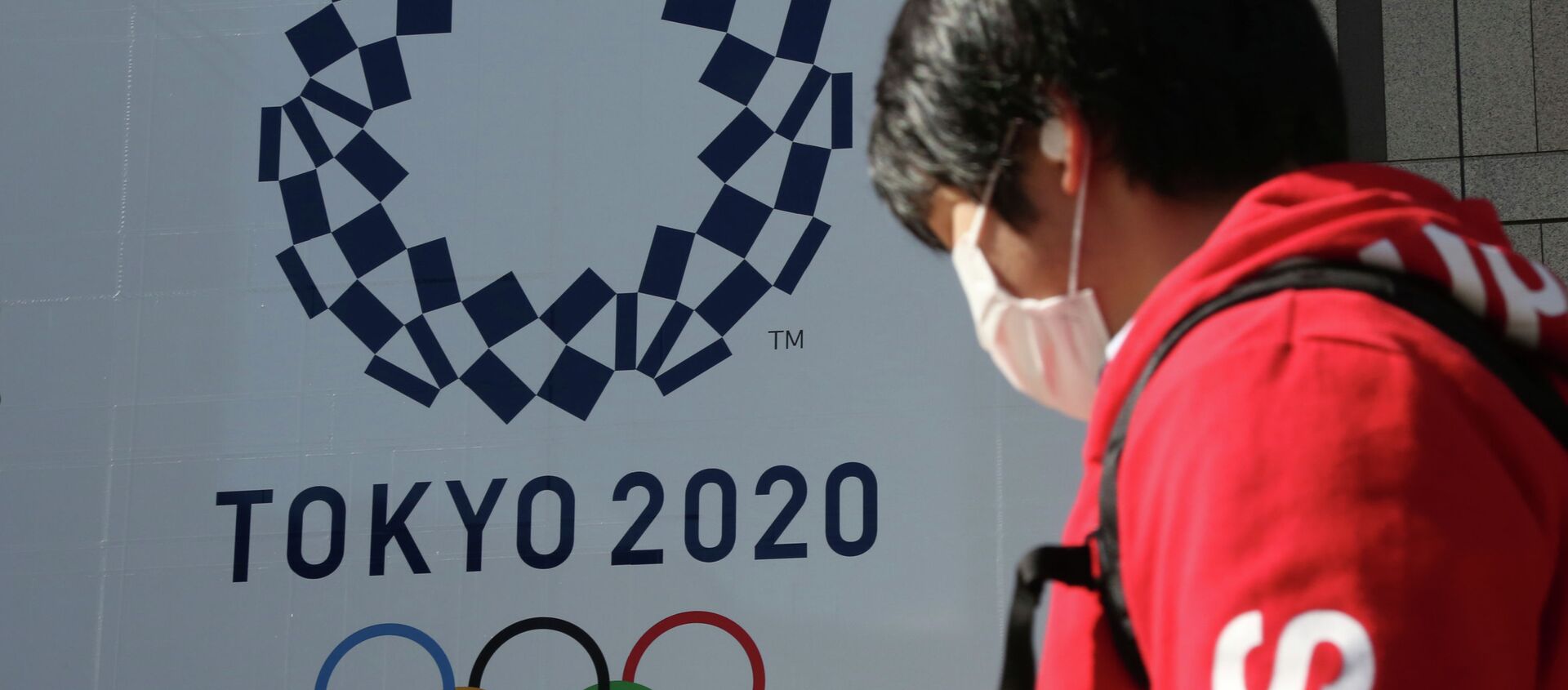 Человек в маске проходит мимо плаката с символикой Олимпиады в Токио  - Sputnik Казахстан, 1920, 09.03.2021