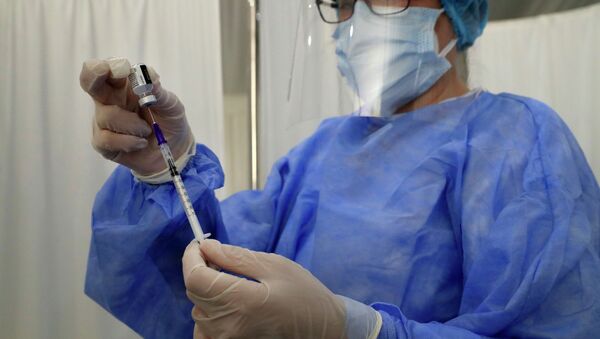 Медик в защитном костюме набирает вакцину в шприц  - Sputnik Казахстан
