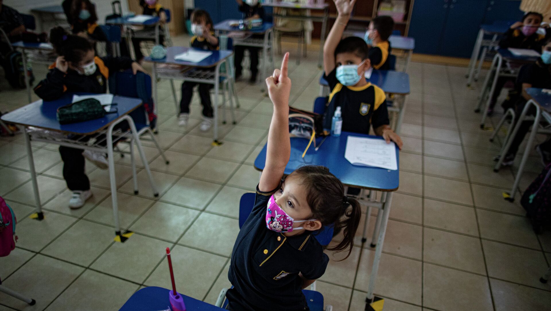 Девочка в защитной маске поднимает руку для ответа на уроке в классе  - Sputnik Қазақстан, 1920, 08.09.2021