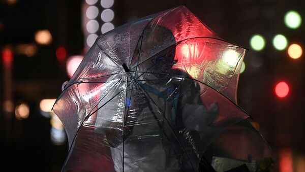 Мужчина в маске укрывается под прозрачным зонтом от ветра вечером  - Sputnik Қазақстан
