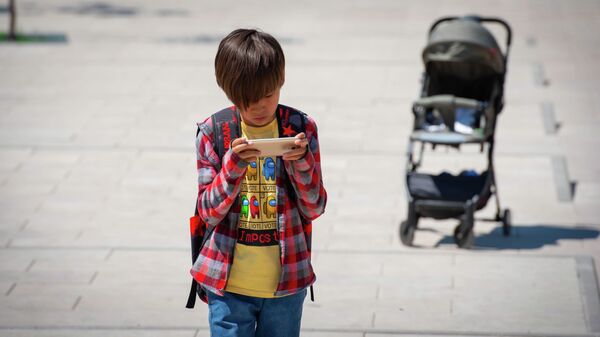 Мальчик идет по улице с телефоном в руках - Sputnik Қазақстан