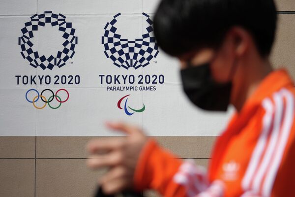 Мальчик в маске проходит мимо логотипов Олимпиады в Токио - Sputnik Қазақстан