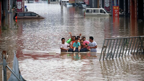Взрослые перевозят детей на надувном матрасе в затопленном после наводнения городском районе в Китае  - Sputnik Казахстан