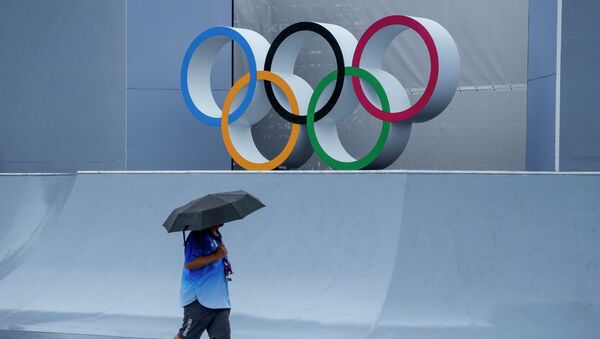 Человек под зонтом проходит мимо олимпийских колец в Токио - Sputnik Қазақстан