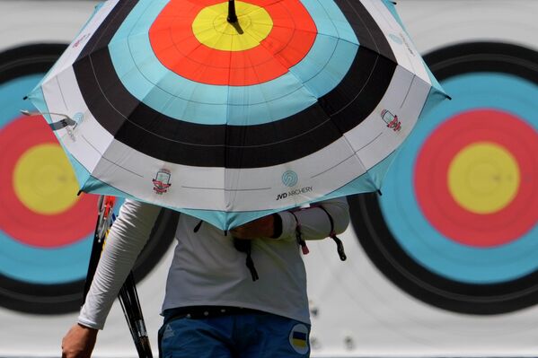 Стрелок из лука прогуливается под зонтом с изображением мишени на Олимпиаде в Токио - Sputnik Казахстан