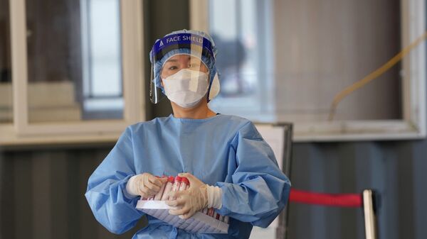 Медик в защитном костюме несет подставку с пробирками ПЦР-тестов на коронавирус  - Sputnik Казахстан