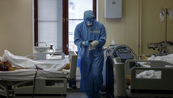 Медик в защитном костюме смотрит на показатели пациентов реанимации в больнице с коронавирусом - Sputnik Қазақстан