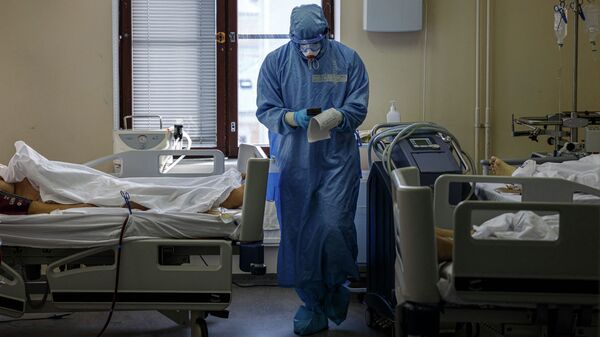 Медик в защитном костюме смотрит на показатели пациентов реанимации в больнице с коронавирусом - Sputnik Қазақстан