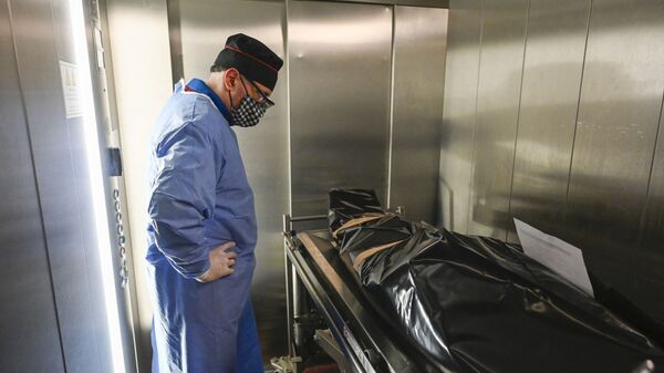Врач стоит радом с носилками, на котором лежит упакованное в пластиковый пакет тело погибшего от коронавируса пациента - Sputnik Казахстан