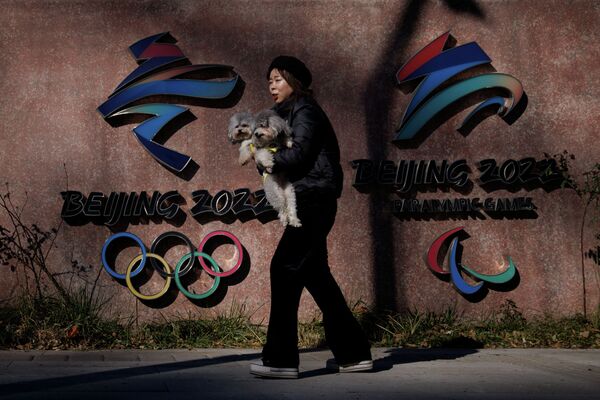 Женщина идет с собакой на руках мимо эмблемы Олимпиады в Пекине  - Sputnik Казахстан