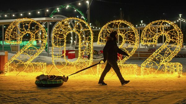 Мужчина везет ребенка на тюбинге мимо новогодней инсталляции  - Sputnik Казахстан