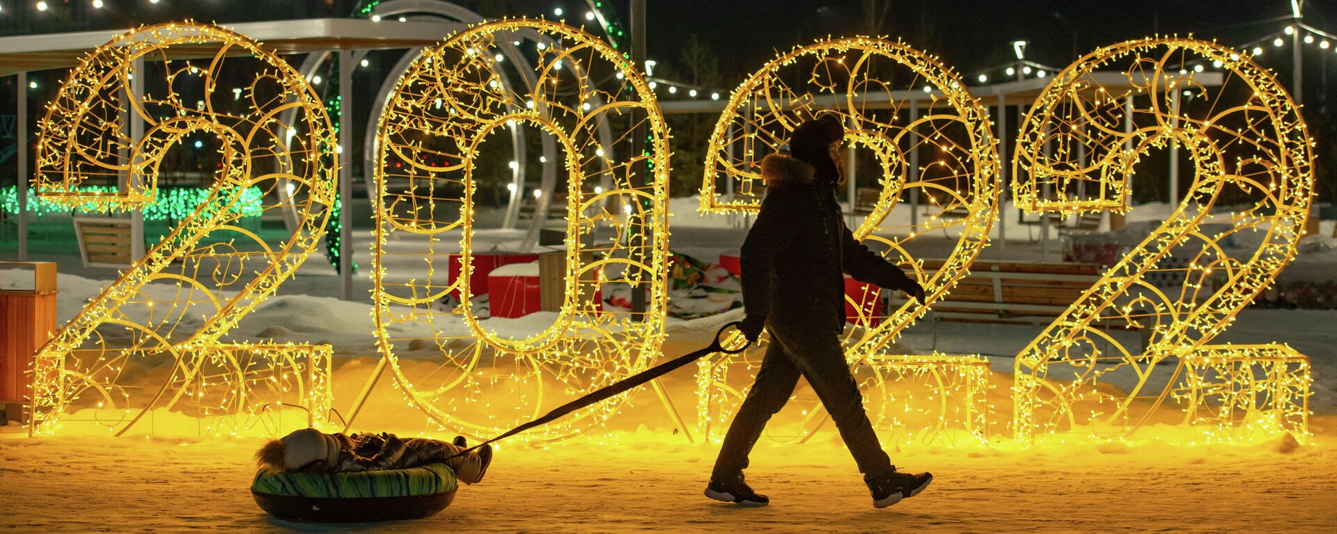 Мужчина везет ребенка на тюбинге мимо новогодней инсталляции  - Sputnik Казахстан, 1920, 01.01.2022